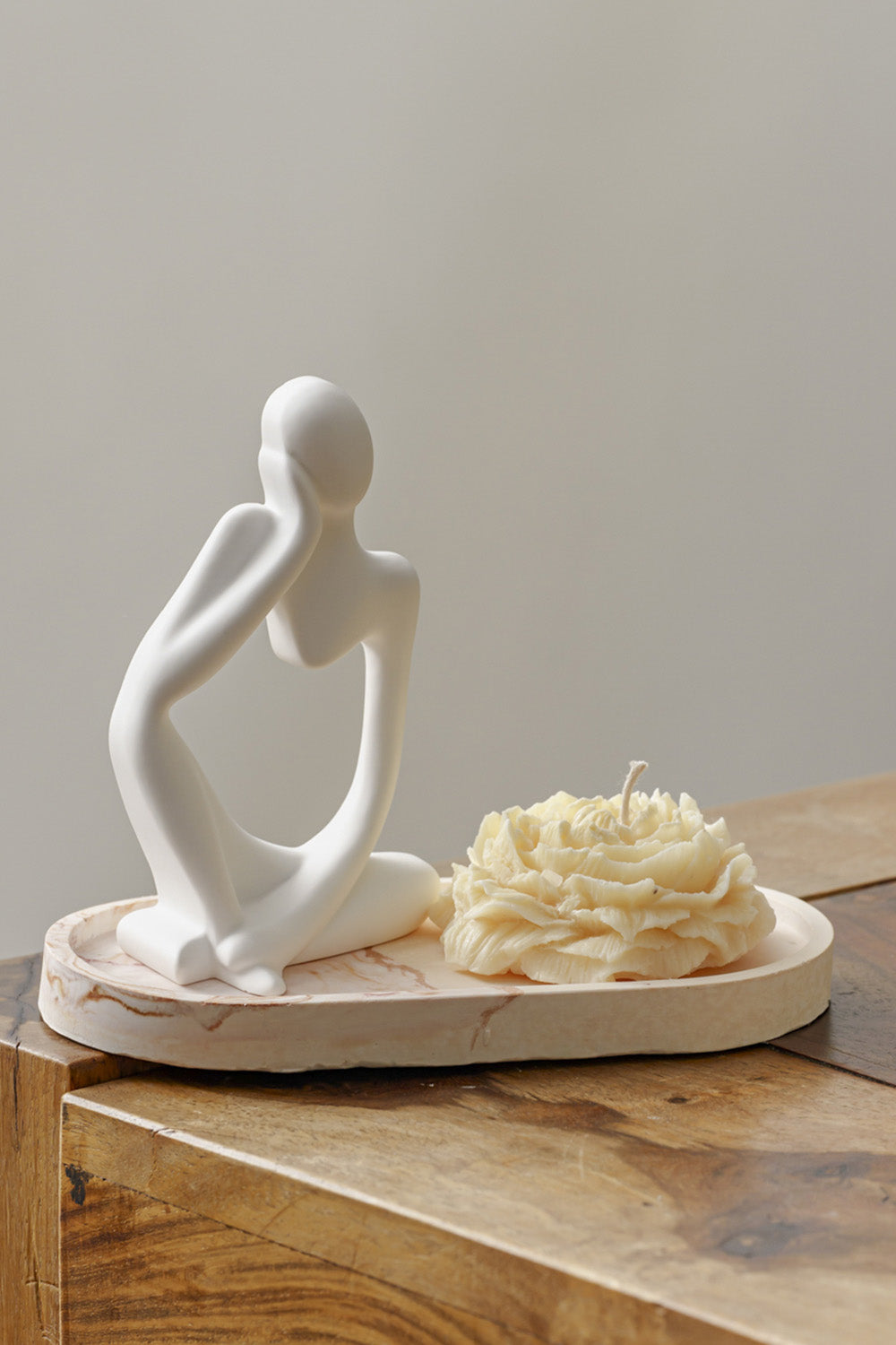 Vela decorativa sobre una bandeja, al lado de una escultura.