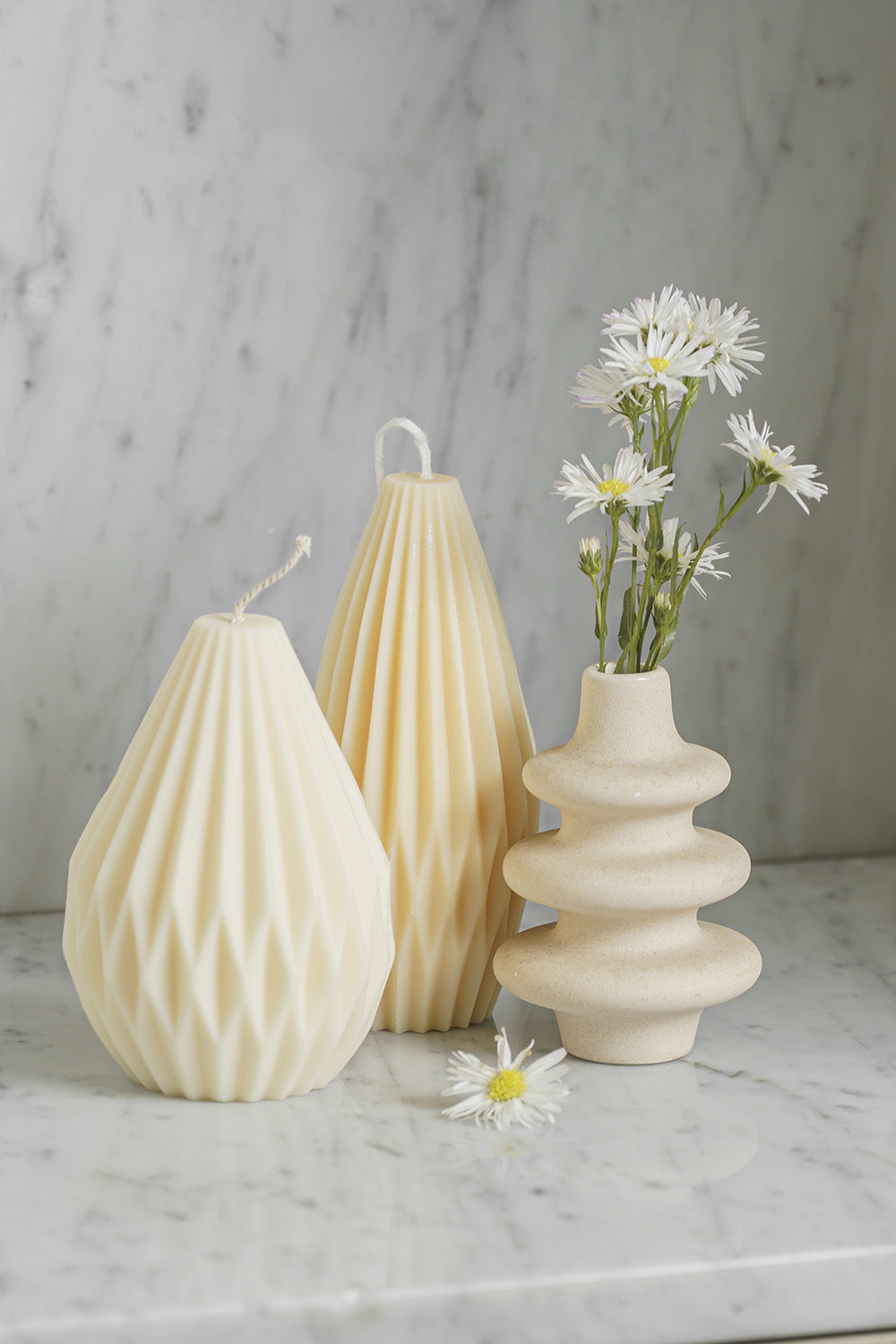 Dos velas decorativas al lado de un jarrón con flores.